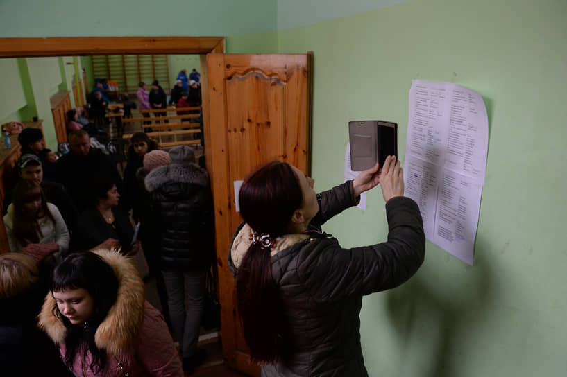 Женщина фотографирует на мобильный телефон списки пропавших без вести при пожаре в торговом центре 26 марта 