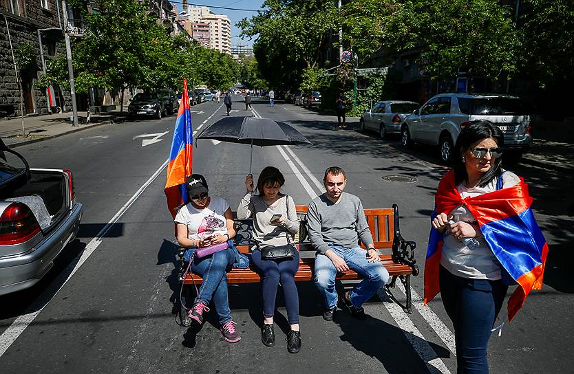 Протестующие сидят на скамейке, блокируя проезжую часть