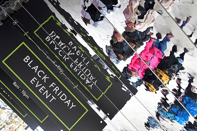 Лондон, Великобритания. Отражение эмблемы «черной пятницы» и посетителей магазинов в лужах на Оксфорд-стрит