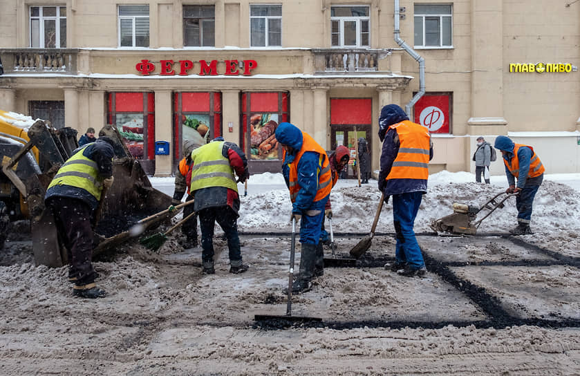 Сотрудники коммунальных служб укладывают асфальт во время снегопада 