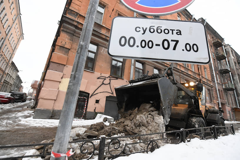 Трактор-погрузчик сгребает снег в кучу у дороги