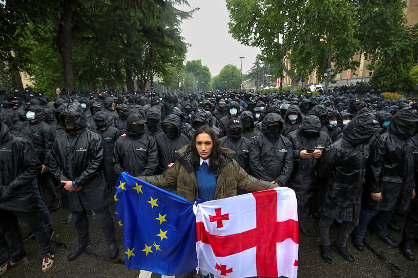 Женщина с флагами ЕС и Грузии перед полицией, блокирующей улицу, чтобы помешать демонстрантам во время акций протеста