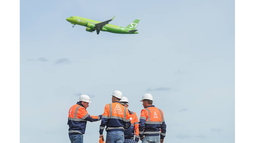 Самолет авиакомпании S7 Airlines взлетает на фоне рабочих компании ОАО «Новосибирскавтодор» во время работ по реконструкции взлётно-посадочной полосы в аэропорту «Толмачево» в Новосибирске 