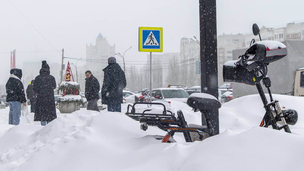 Электровелосипед курьера стоит на улице, занесённый снегом 