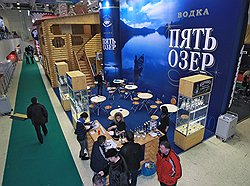 Деревянный сруб на фоне небесно-голубого стенда Алкогольной сибирской группы, очевидно, призван напомнить посетителям о бескрайних русских просторах