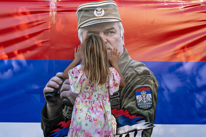 Девочка возле флага с изображением Ратко Младича