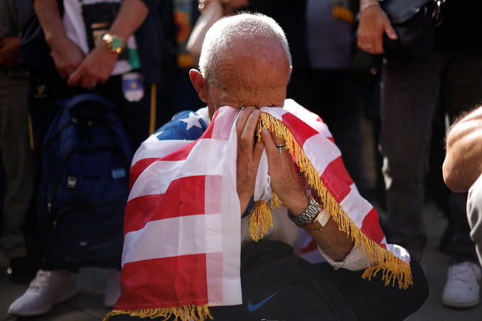 Мужчина вытирает слезы флагом США на митинге в Косово