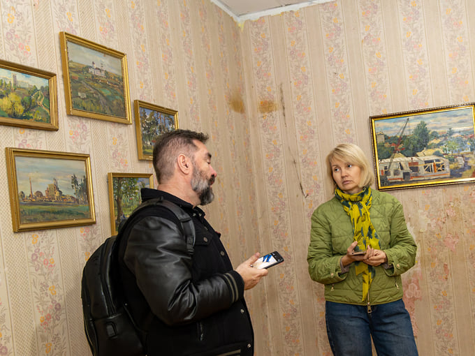 Посетители знакомятся с экспозицией в одной из комнат Дома Фирюпкина. Картины разместили на стенах со старой отделкой, не скрывая следов запустения здания