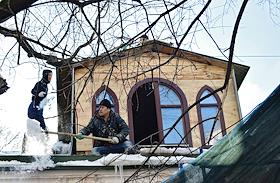Снегопад в городе. Строитель убирает снег с крыши здания